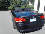 Black 2009 BMW 328i convertible with low mileage parked in a sunny driveway.