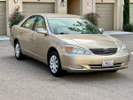 2002 Toyota Camry SE in gold color parked in front of a garage, showcasing its excellent condition and low mileage.