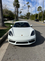 Front view of a white 2018 Porsche 718 Cayman parked on a palm tree-lined street.