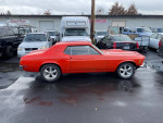 1970 Ford Mustang in red, parked among various vehicles, showcasing its classic design and modern upgrades.