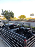 2002 GMC Sierra LB7 truck with a motorcycle in the bed, parked in a modern urban setting.